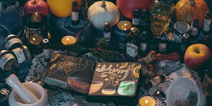 Książka o alchemii na stole z koronkowym obrusem, zastawionym różnymi miksturami oraz świeczkami.