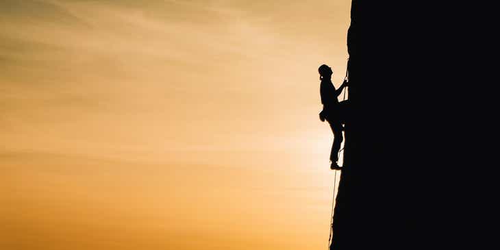 Eine ambitionierte Person besteigt in der Dämmerung eine steile Felswand.
