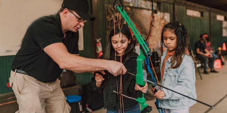 Hombre enseñando a unas niñas a usar un arco en una clase de tiro con arco.