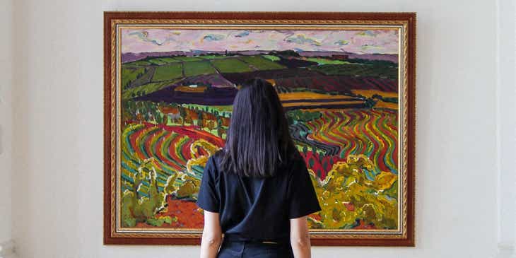 Eine Frau betrachtet ein großes, eingerahmtes Gemälde eines Künstlers in einer Galerie.