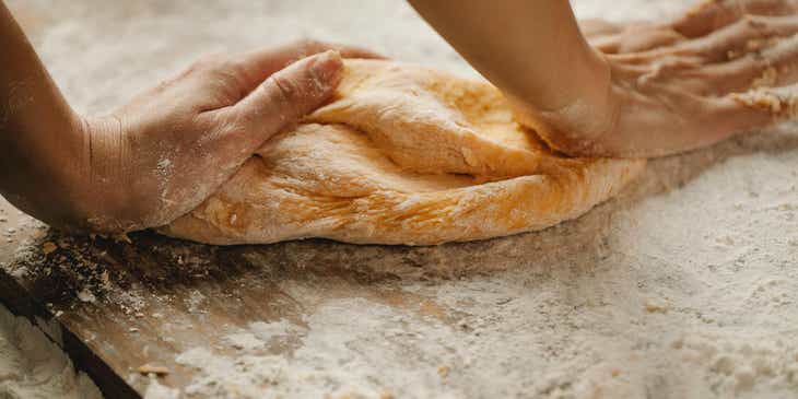Um artesão amassando uma massa de pão com as duas mãos.