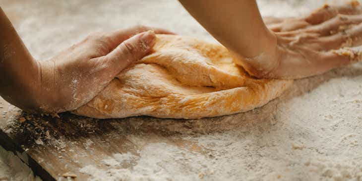 Seorang artisan roti sedang menguleni adonan dengan kedua tangannya.