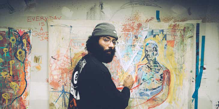 An artist working on a canvas against a wall covered in graffiti.