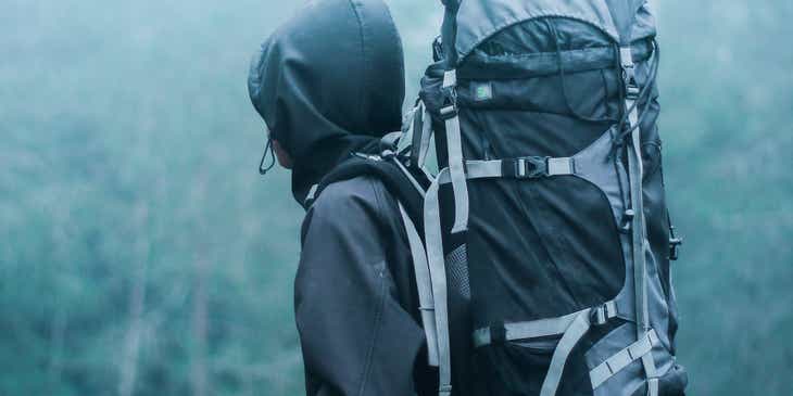 Seorang backpacker sedang berdiri di tengah hutan berkabut.