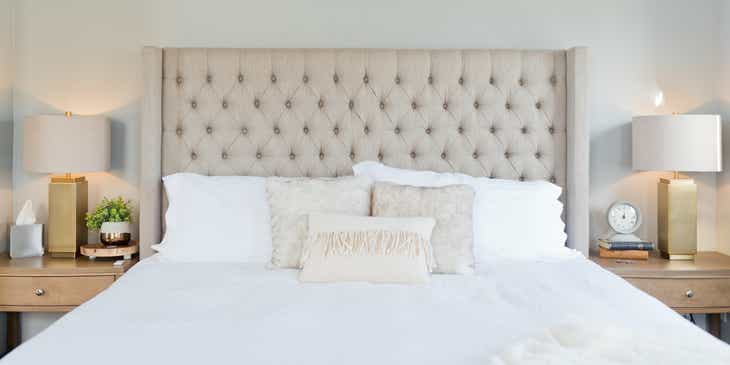 Ein Doppelbett mit einem stoffbezogenen Kopfteil, verschieden großen Kissen und weißem Überzug in einem Bettengeschäft.
