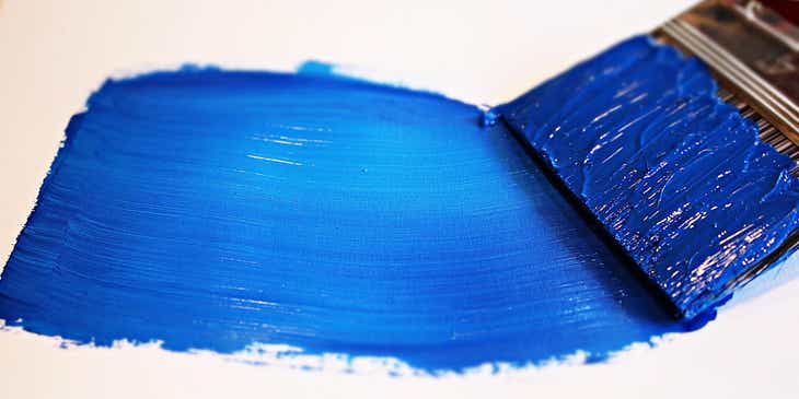Blaue Farbe wird mit einem breiten Pinsel auf eine weiße Oberfläche aufgetragen.