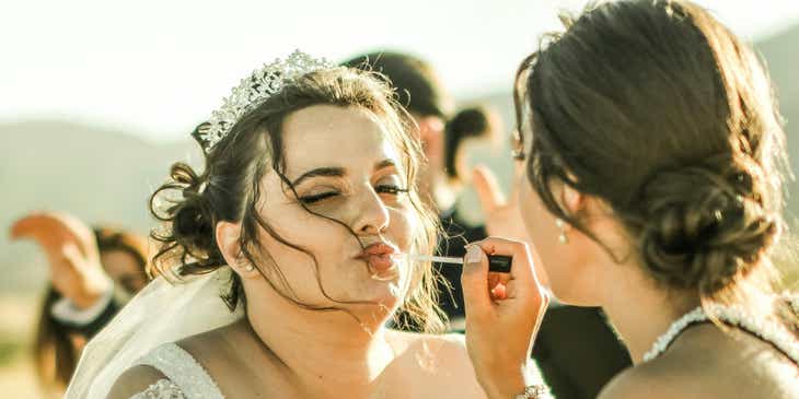 Uma maquiadora retocando a maquiagem de uma noiva.
