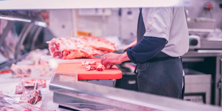 Een slager die vers vlees snijdt in een slagerij.