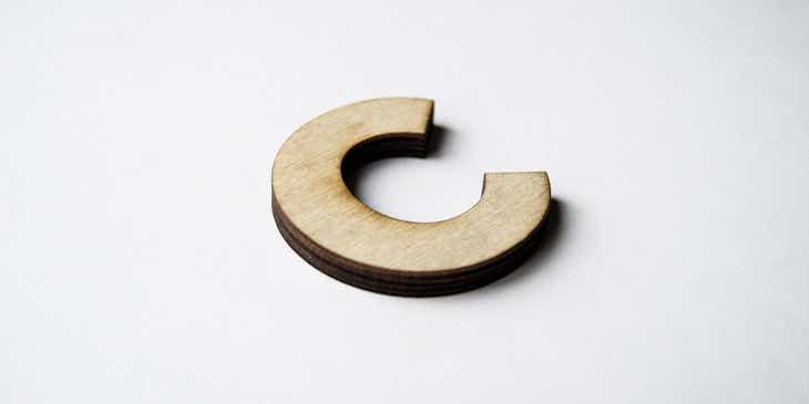 Letra C feita de madeira em cima de uma superfície branca.