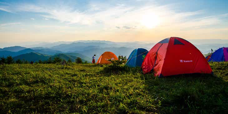 Bunte Zelte auf der Wiese eines Campingplatzes mit Blick auf die umliegenden Berge.