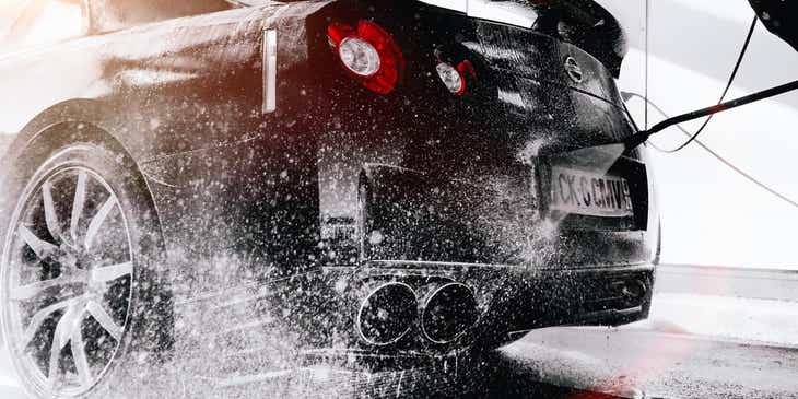 Czarny samochód opłukiwany wodą podczas mycia w myjni samochodowej.