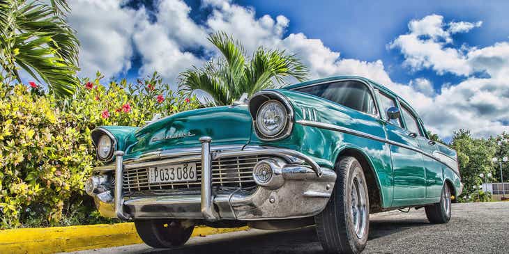 A classic blue car pictured against a bright blue sky and palm trees.