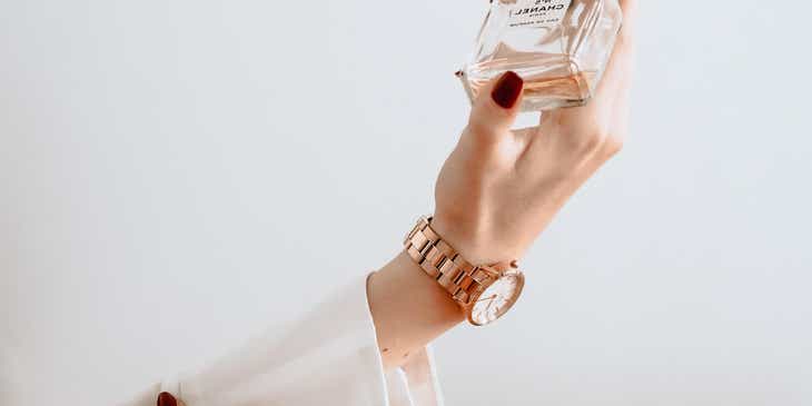 De hand van een stijlvol persoon die een fles parfum vasthoudt.