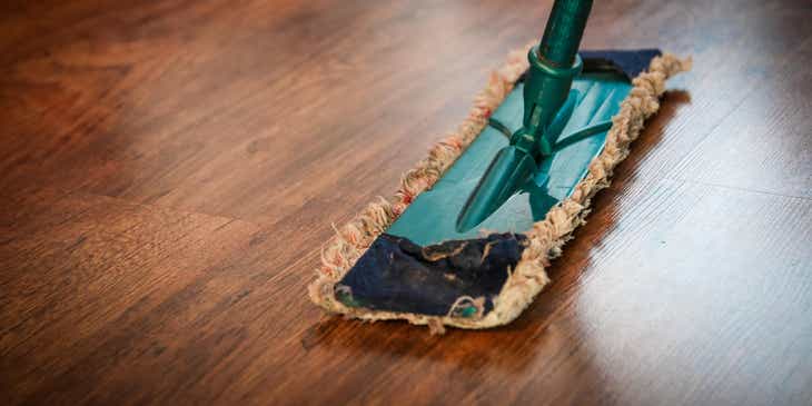 Een persoon maakt een houten vloer schoon met een dweil.