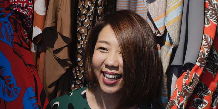 Mujer sonriente de pie entre bastidores de ropa en un logo para tiendas de ropa.