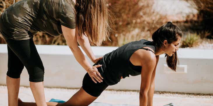 Una coach che aiuta una donna durante la sua attività di coaching di yoga.