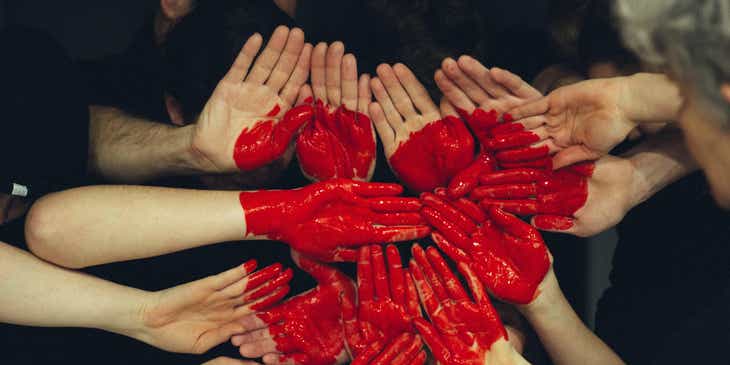 Mitarbeiter eines Wohltätigkeitvereins haben ihre Hände mit roter Farbe in der Form eines Herzens angemalt, um Solidarität und Fürsorge zu zeigen.
