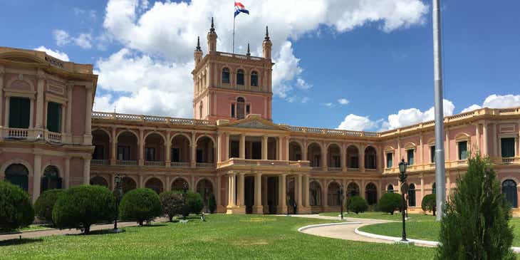 Un edificio de gobierno con un enorme jardín y la bandera de Paraguay en el techo.