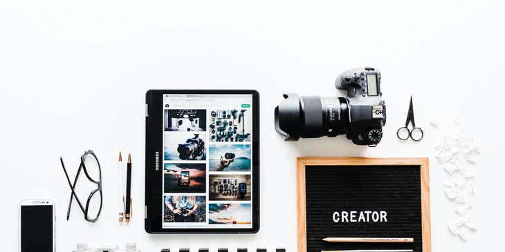 Eine Auswahl an Arbeitsmaterialien für ein Kreativdesignstudio, wie unter anderem ein Handy, Stifte, Kameras, vor einem weißen Hintergrund.
