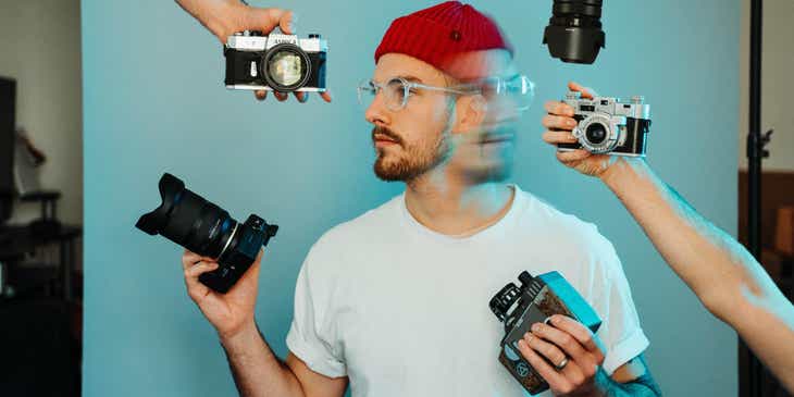 Fotograf działający w branży kreatywnej otoczony rękoma podającymi różne kamery.