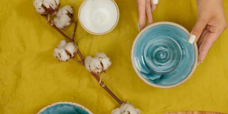 A person placing blue and white ceramic bowls used as crockery on a yellow table cloth next to a cotton frond.