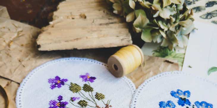 Various cross-stitch floral designs with spools and scissors on a table.