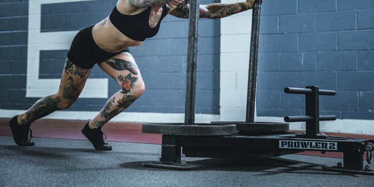 Een getatoeëerde vrouw die trainingsmateriaal vooruit duwt in een CrossFit sportschool.