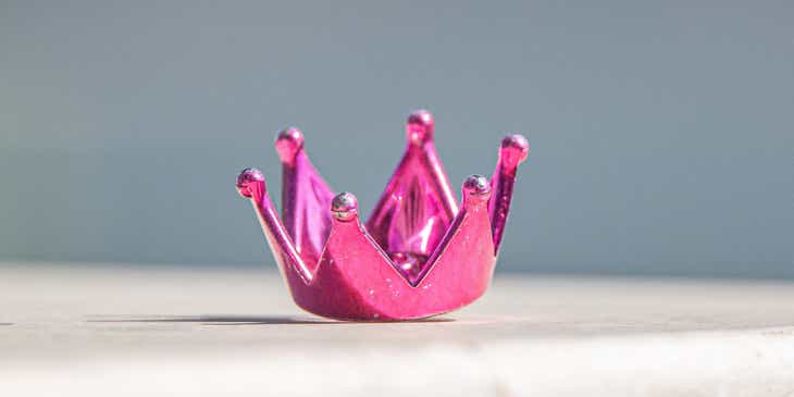 Zabawkowa, różowa korona leżąca na blacie.