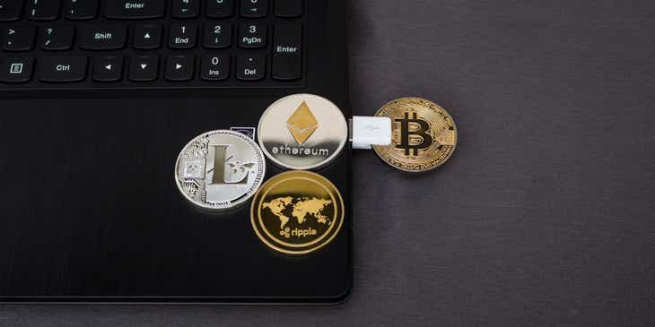 Münzen mit den Logos bekannter Kryptowährungen liegen auf einem Laptop.