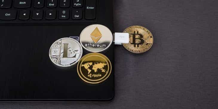 Delle monete che rappresentano diverse criptovalute — Ripple, Litecoin, Bitcoin ed Ethereum — disposte sopra un pc.