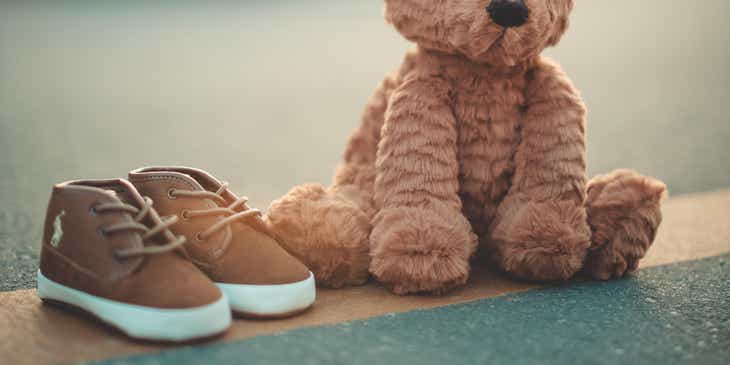 A tiny pair of shoes next to a cute teddy bear.