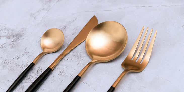 Gold and black cutlery on a marble counter.