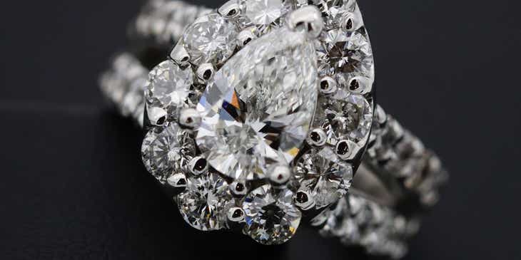 Um anel cravejado de diamante prateado contra um fundo escuro.