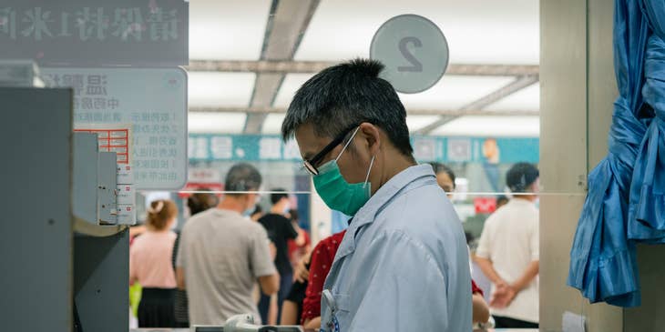 A doctor wearing a white lab coat and face mask sorting through medicines.