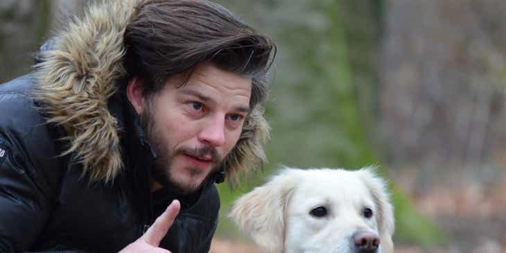Ein Mann kniet neben seinem Hund im Wald und achtet auf die Anweisungen eines Hundetrainers.