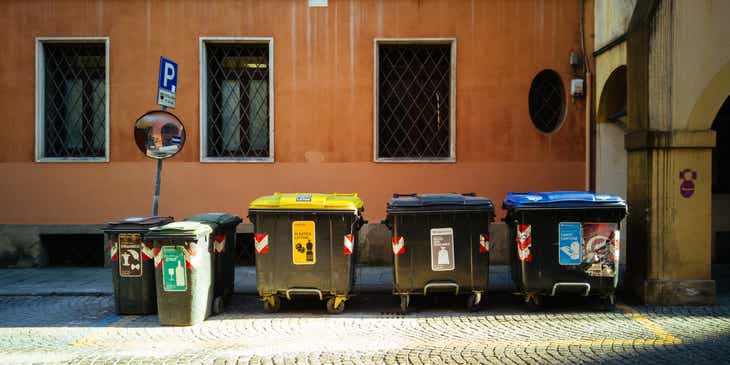 Pojemniki na różnego rodzaju odpady stojące przed budynkiem, czekające na na odbiór śmieci.