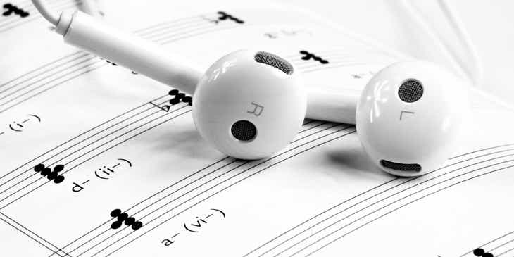 A pair of white earphones lying on top of a music score sheet.