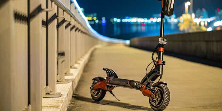 A red and black electric scooter parked on a bridge.