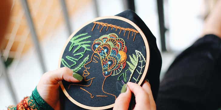 An woman stitches a design onto the backing of an embroidery hoop.