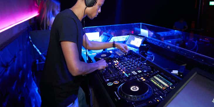 Seorang DJ yang sedang mengoperasikan peralatan musik elektronik untuk sebuah bisnis hiburan.