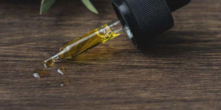 Eine Glaspipette mit einem ätherischen Öl liegt auf einem Holztisch.