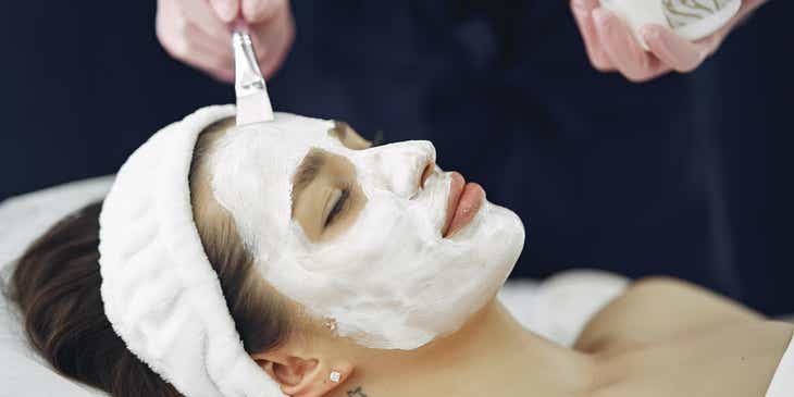 Eine Frau lässt sich in einem Schönheitssalon eine weiße Gesichtsmaske auftragen.