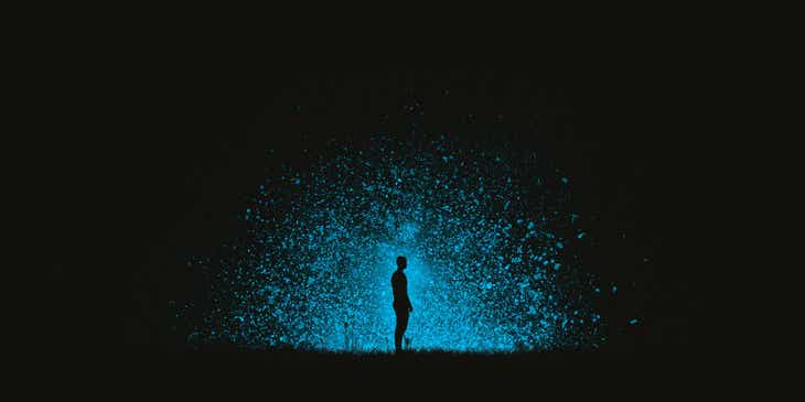 Mężczyzna stojący w ciemnościach na tle niebieskiego wybuchu.