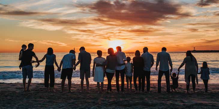 A large family standing together and facing the ocean at sunset.