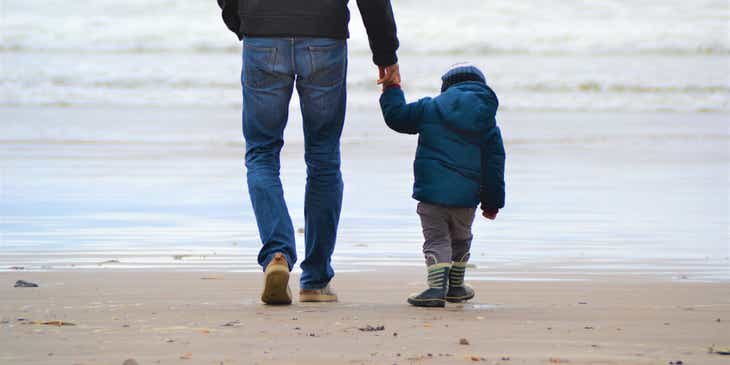 A father and son walking on a beach.