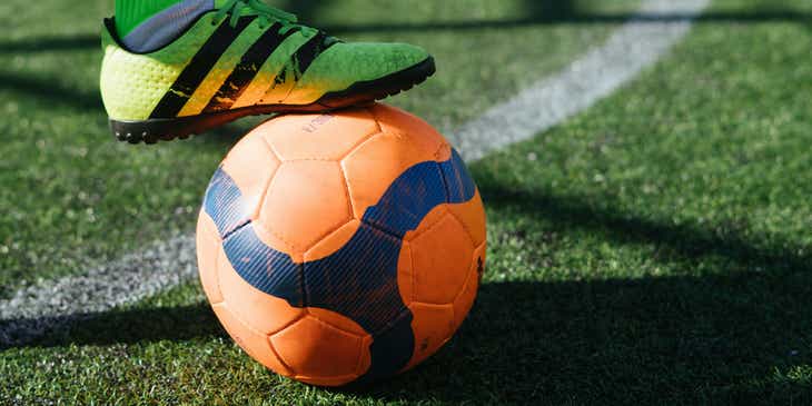Ein Fußballspieler stoppt einen orangen Ball mit seinem Schuh.