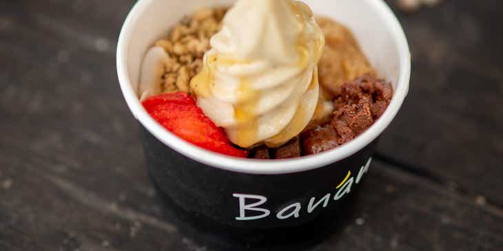 A cup of frozen yogurt topped with granola, honey, and fresh fruit.