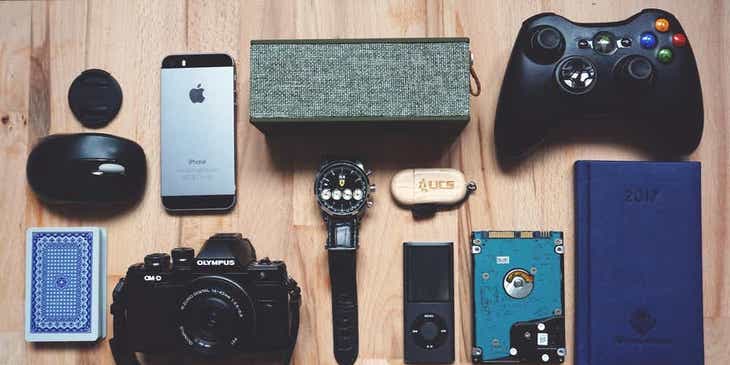 Verschiedene Gadgets – vom Smartphone bis zum Gamecontroller – liegen auf einem Holztisch.