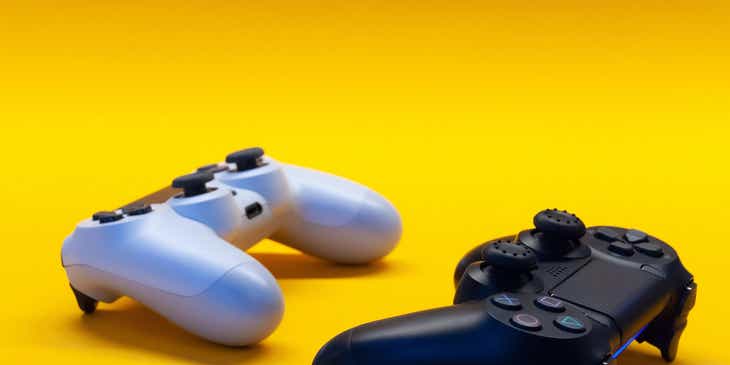 Due controller per videogiochi, venduti da un'azienda di gaming e disposti su un piano giallo.