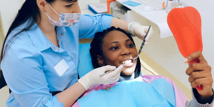 Eine Zahnärztin zeigt einer Patientin, die einen Handspiegel hält, ihre Zähne während einer Behandlung.